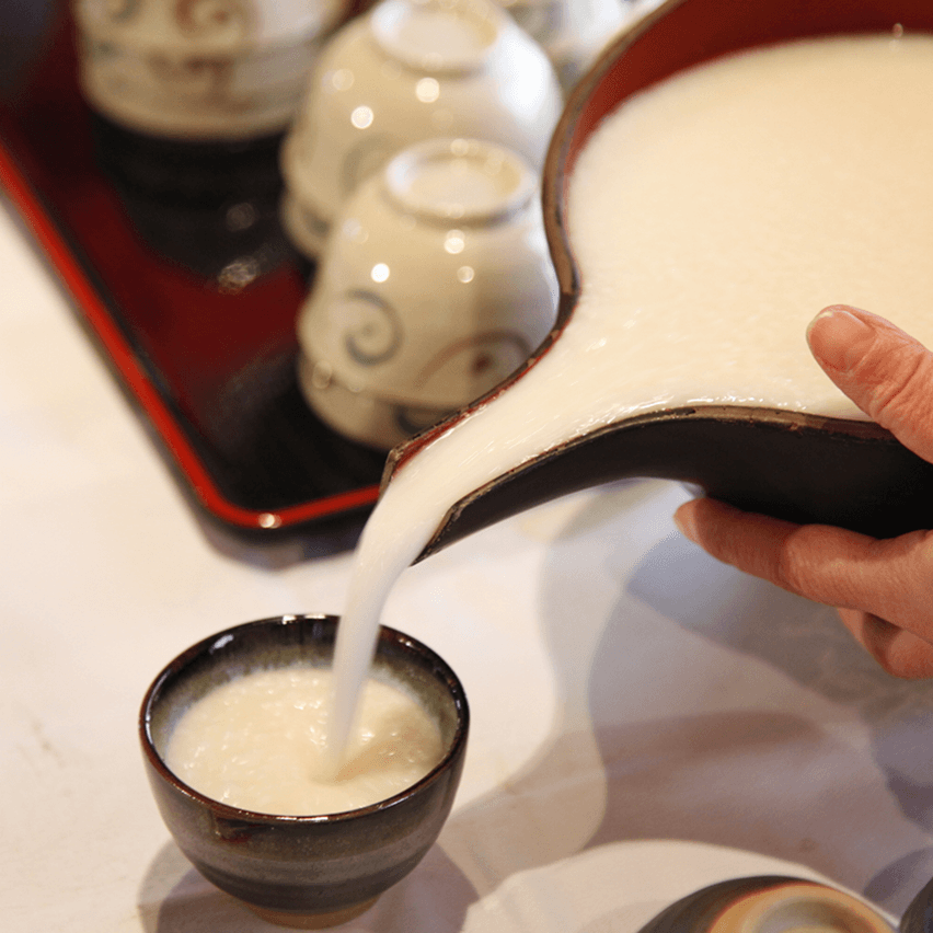 どぶろくを器から小さな茶碗に注いでいる様子